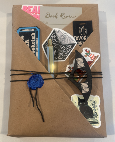A wrapped blind date with a book with stickers, a pen, a book review card, and a reading accessory